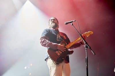 A musician plays guitar onstage in a large music venue