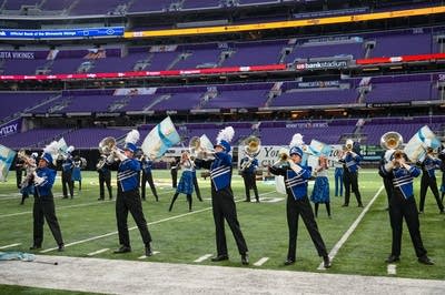 A marching band performs on the field of a football stadium.