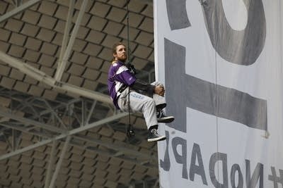 A protester hangs from the grid of US Bank Stadium