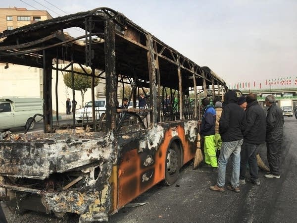 Iranians inspect the wreckage of a bus that was set ablaze by protesters during a demonstration against a rise in gasoline prices in the central city of Isfahan (Credit: Getty Images).