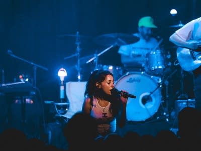 A woman sings into a microphone on a lighted stage.