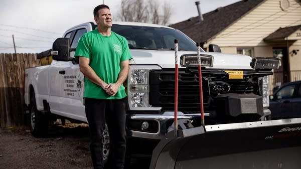 A person stands next to a snow plow truck