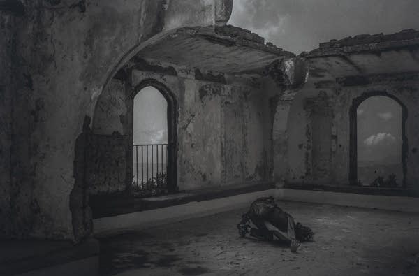 A black and white photograph of a person in a worn down building.