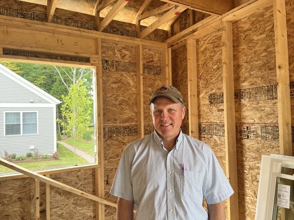 A man in a baseball cap stands inside a home under construction.