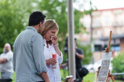 A woman wipes away tears while she and a man look at photos at a vigil.