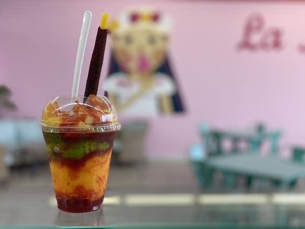 a plastic cup holds red, green and orange sorbet