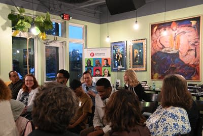 People gather in a space in the restaurant as one woman stands holding a microphone.