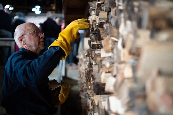 A man pulls firewood out of a wall of wood. 