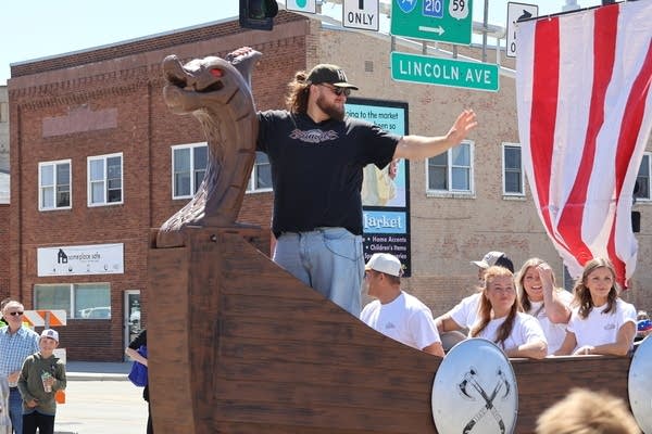 A man waves from a parade float modeled after a viking ship.