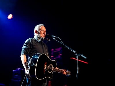 Bruce Springsteen sings into a microphone while playing a guitar.
