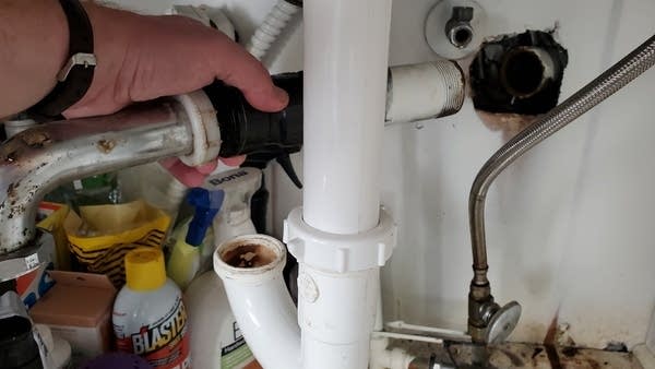 Photo of Andrew's hand holding a disconnected pipe under kitchen sink