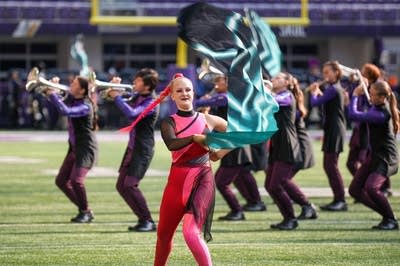 A marching band performs on the field of a football stadium.