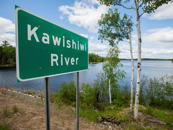 A green sign is located along the banks of the Kawishiwi River.