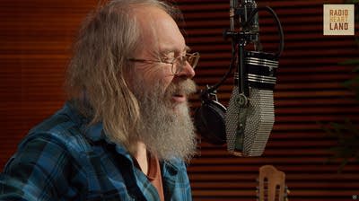 A musician sings and plays guitar in a recording studio
