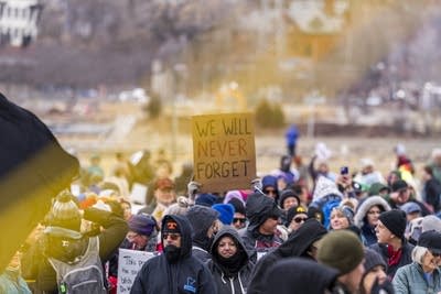 Someone holds a sign that says we will never forget