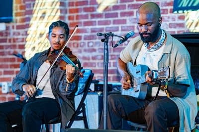 One musician plays a resonator guitar while another plays fiddle