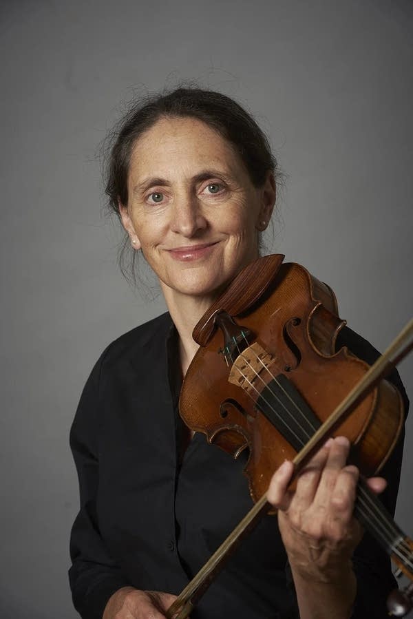 A musician smiles while holding a violin