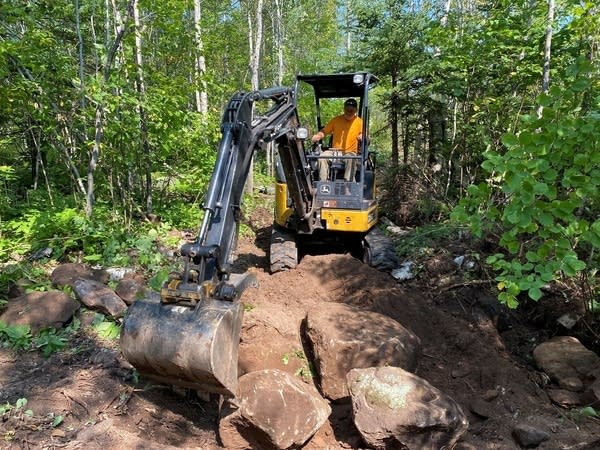 A person uses an excavator to move rocks. 