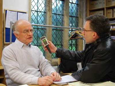 John Birge holds a microphone device up to a man's face.