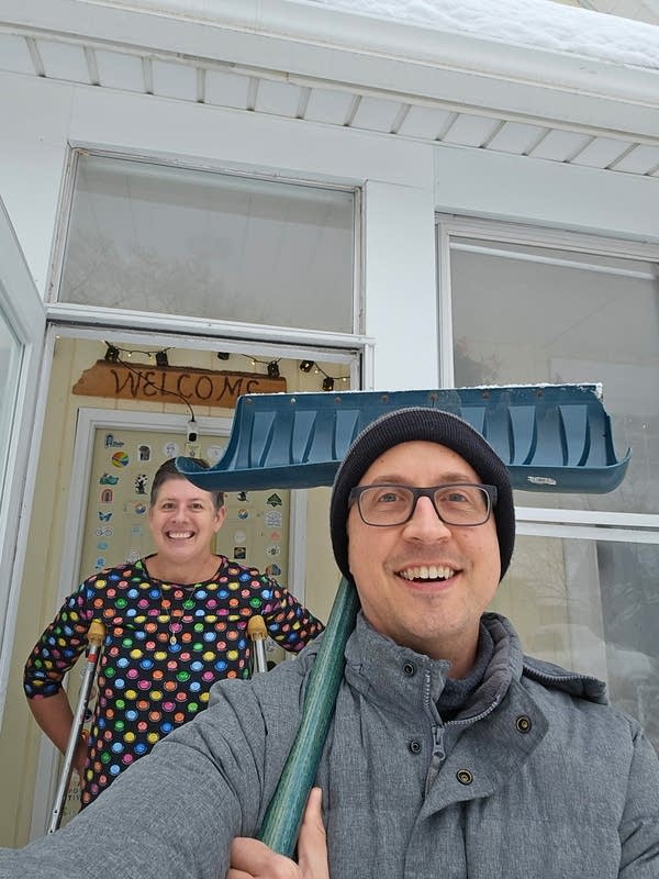 Two people pose with a snow shovel