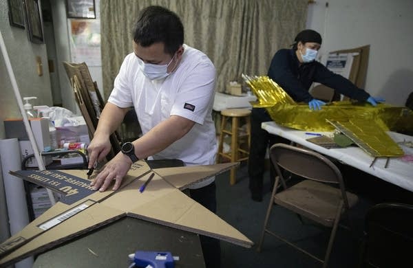 A man wearing a face mask cuts large cardboard into a star.