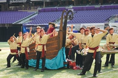 A marching band performs on the field of a football stadium.