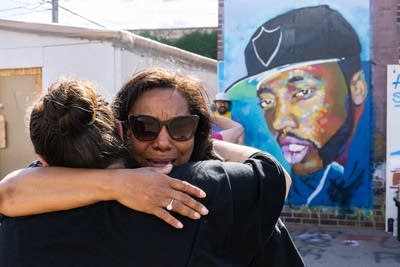 Two women hug in front of a painting. 