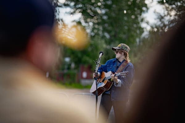 A musician sings and plays guitar on an outdoor stage