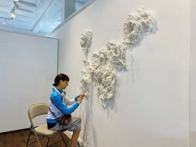 A woman works to install a piece of art on the wall.