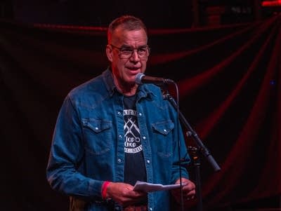 A man wearing a denim shirt speaks into a microphone.