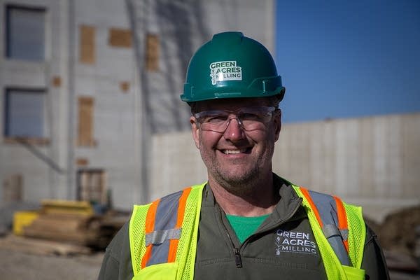 A man in a construction hat and hi-vis vest smiles for a photo.
