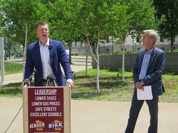 A man speaks at a podium as another man listens