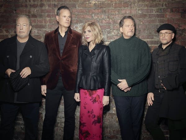Five people stand against a brick wall.