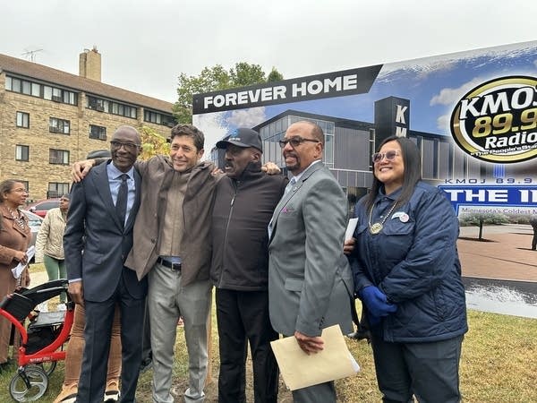 Five people pose for a photograph in front of a new sign.