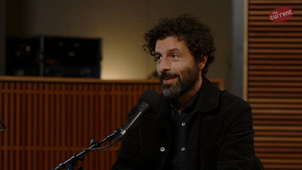 A musician smiles while speaking to another person in a recording studio