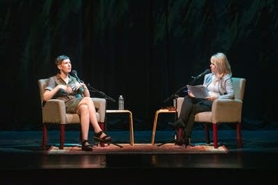 Author Patricia Lockwood and host Kerri Miller converse while sitting in beige armchairs on a large, dark stage.