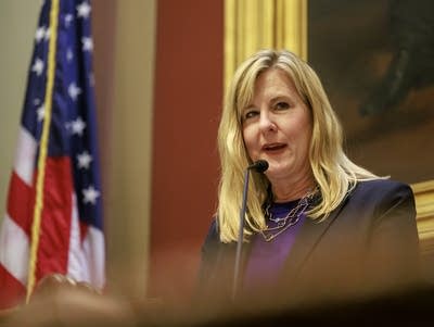 woman speaking on a microphone with the U.S flag 