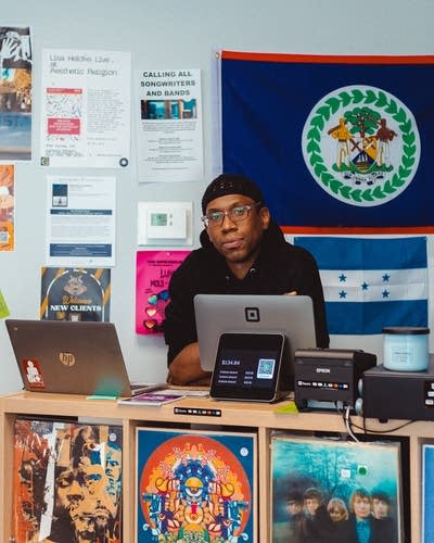 A man sits at a counter by a cash register in the shop he owns