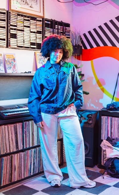 A person stands by shelves of records while wearing a vintage jacket
