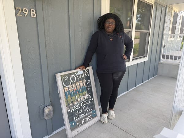 A woman poses for a photo on the porch of a newly built house.