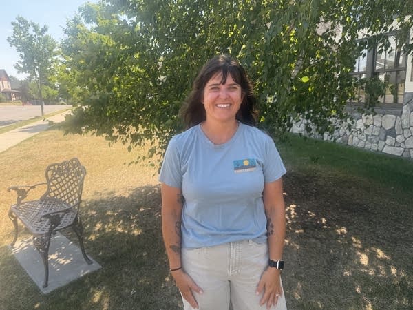 A woman in a light blue shirt smiles for a photo in front of a tree.