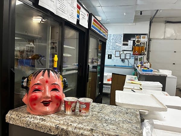 A counter with a jar resembling a face, two cups, and refrigerators.