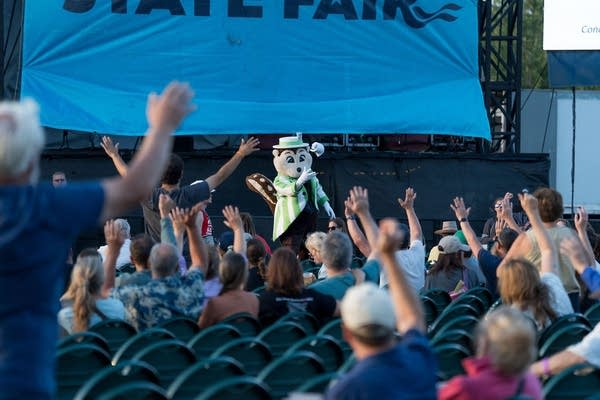 People interact with a costumed mascot at an outdoor music venue