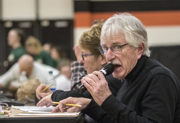 A man speaks into a microphone in a high school gym.