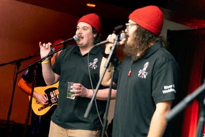 Men wearing red beanies talking into microphone