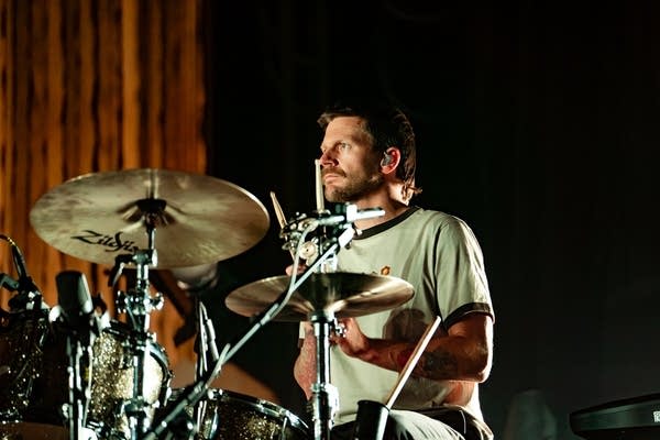 A man plays drums onstage in a large music venue
