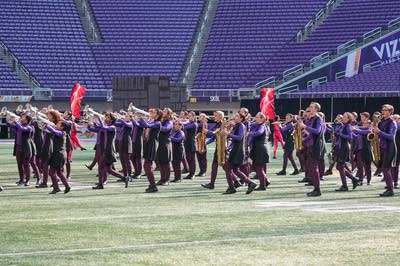A marching band performs on the field of a football stadium.