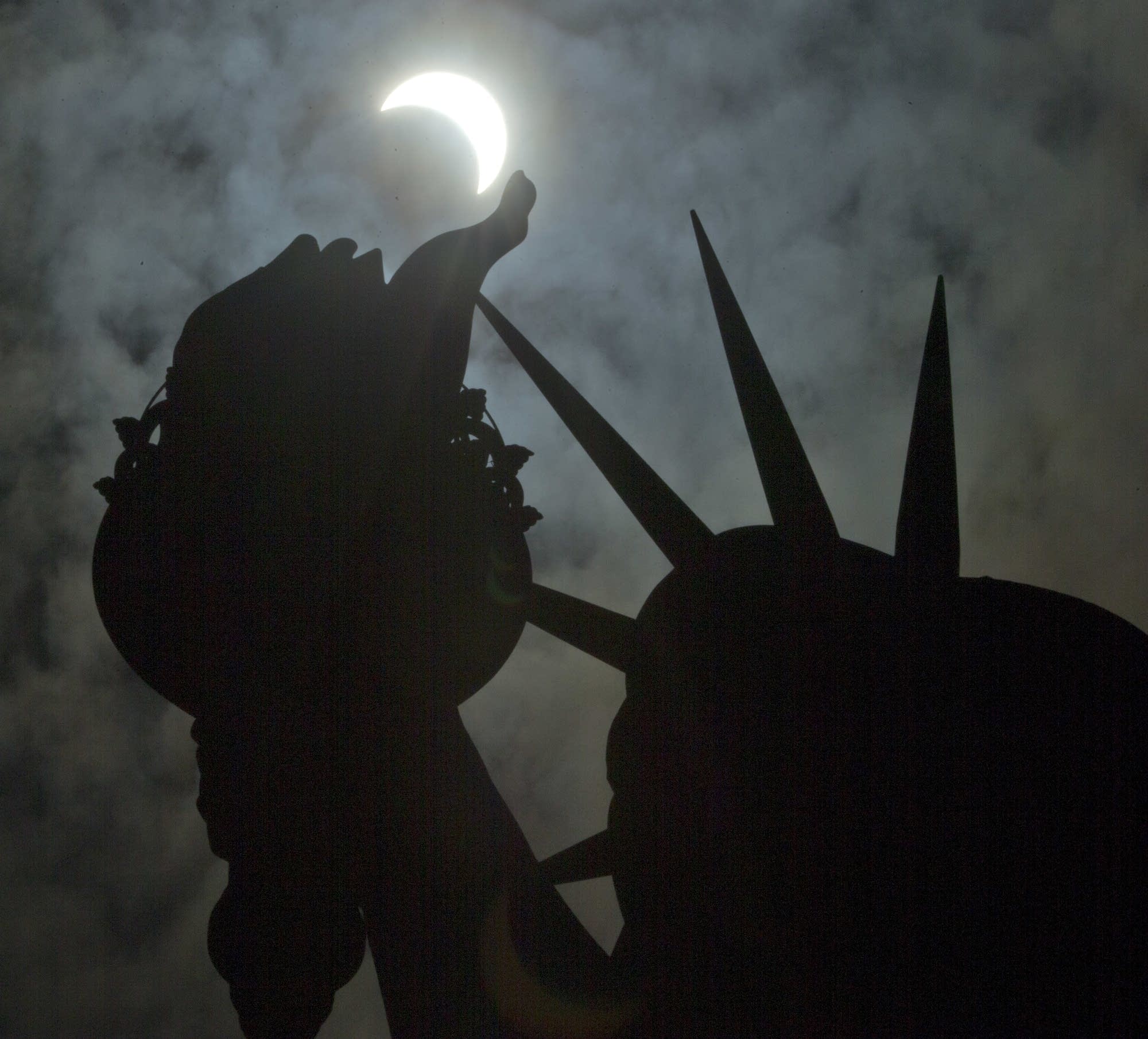 A view of the partial solar eclipse hangs above the Statue of Liberty.