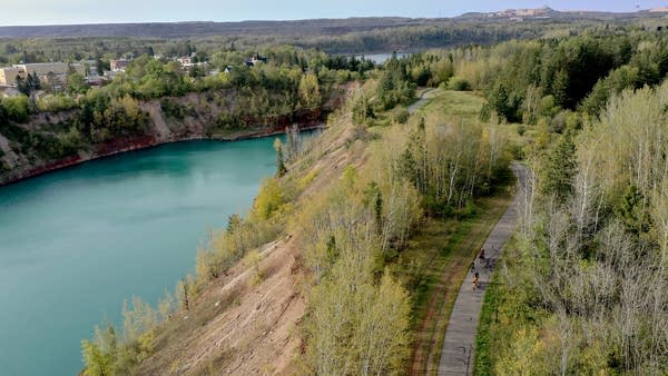 Aerial view of a forest trail running alongside a mining pit filled with water.