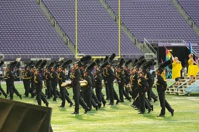 A marching band performs on the field of a football stadium.